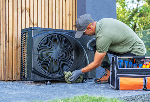 A technician fixes a ceiling AC unit with a screwdriver.