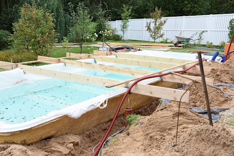 This image shows an outdoor pool under construction in the back yard of someone's home. 