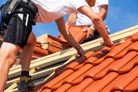 Closeup of two roofers installing a new orange-red tiled roof.
