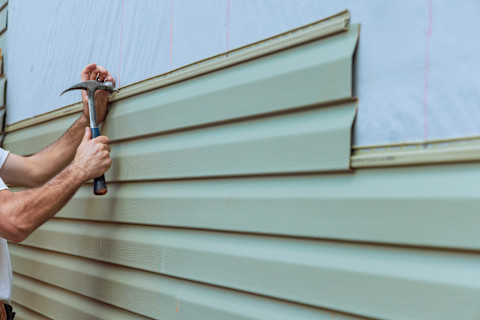 Vinyl siding installation in progress, improving home exterior protection and insulation. The contractor secures siding panels to the wall framework, ensuring weather resistance and energy efficiency. Exterior siding enhances curb appeal while safeguarding against moisture and temperature fluctuations.
