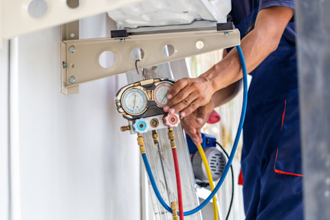 A technician fixes an air conditioning unit and checks the level of refrigerant.