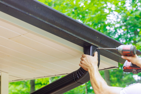 This image shows a person removing leaves and debris from guttering.