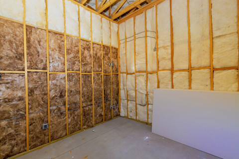 A room under construction, with two perpendicular open walls featuring two different kinds of insulation.