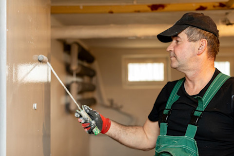 A professional painter works on a wall in a basement undergoing renovation.