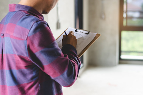 This image shows a tradesperson with a clipboard and pen carrying out a home inspection.