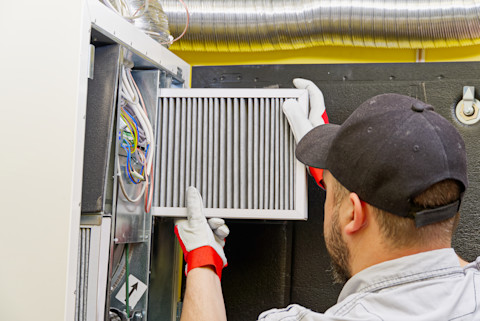 This image shows an HVAC technician wearing gloves to remove or change a furnace filter.