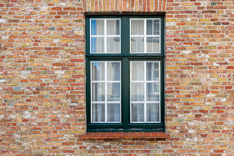 A vintage brick wall facade with a window in Bruges is shown. The aged bricks and window frame reflect historic architecture.
