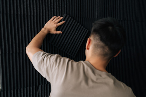  Rear angle of a man installing acoustic foam panels on a wall.