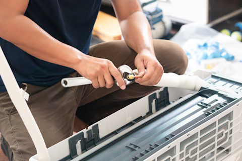 A worker uses a wrench to fix joints and copper piping in an air conditioning unit.