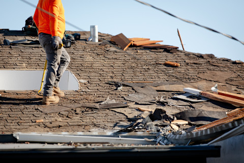 A roof repair pro stands on a roof where a large section has been visibly damaged. Different repair materials are spread out across the roof.