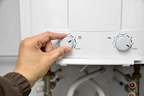 Closeup of a hand turning a knob on a water heater.