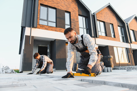 Paving contractors lay stones on a new pathway. The ground is prepared for even placement.