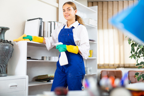 A cleaner is working in a home with cleaning supplies and gloves