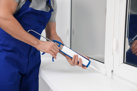 A pro uses a caulking gun to seal a window.