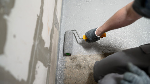 A worker wearing a highlight uses a pipe wrench to fix a leak in a brick wall.
