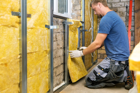 A worker insulates an old brick wall with mineral wool.