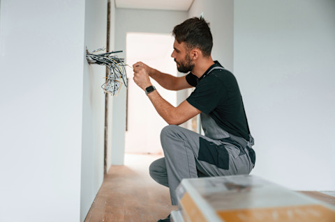 A man is installing electrical wiring in a new home.
