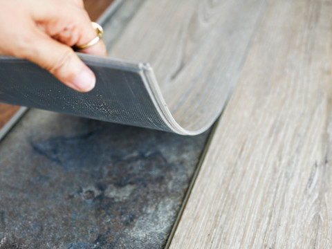 Closeup of a vinyl flooring panel being installed over floor tiles.