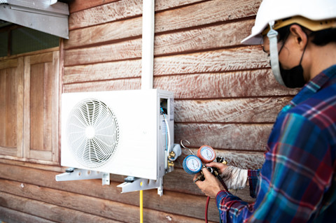 Outside a house, a workers installs and refills the exterior part of an air conditioning unit.