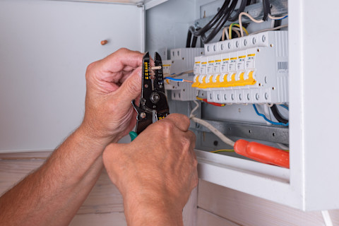 An electrician uses a wire stripper to prepare a circuit wire inside an open residential breaker panel.