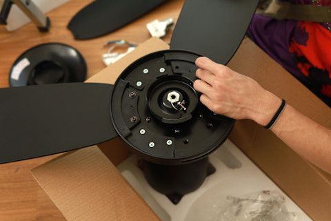 Downwards shot of the interior of a black ceiling fan that’s still in its box. A hand is visible over the fan.
