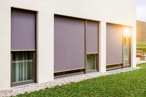 Exterior shot of the side of a home, with four windows featured ceiling-to-floor shades pulled down either fully or halfway.
