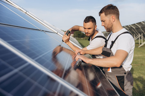 Two pros install solar panels in a field.