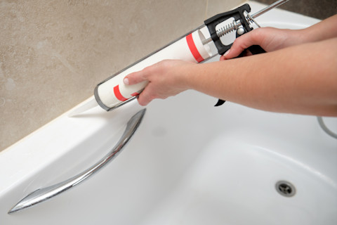 A worker uses a caulking gun to apply sealant around a bathtub.