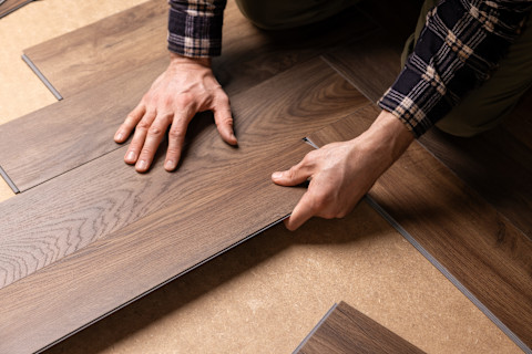 Closeup of a worker’s hands installing vinyl wood flooring over a smooth subfloor.