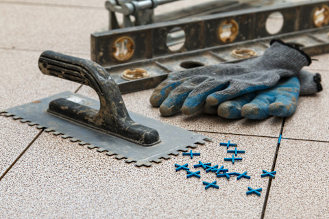 Closeup of gloves and different flooring tools on ceramic tiles.