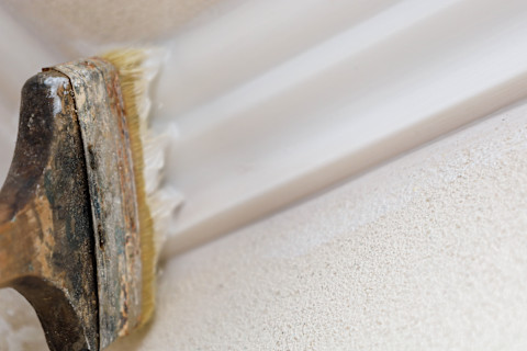 Closeup of a wide brush painting a stucco ceiling and moulding white.