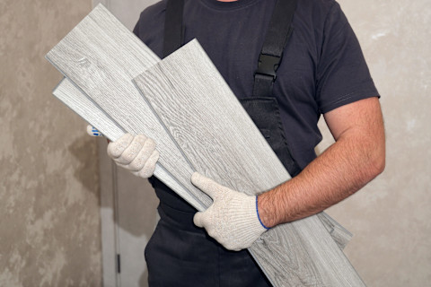 A worker carries grey vinyl flooring planks for installation.