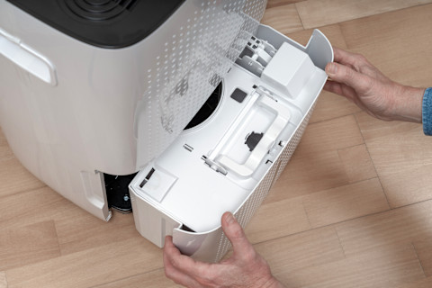 Closeup of a homeowner’s hands removing a tank from a home dehumidifier.