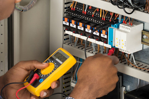 Closeup of hands with a multimeter. A pro is using it to check a fuse box.