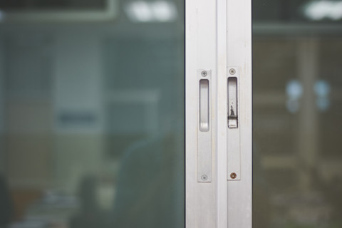 Closeup of a frosted sliding door with a metal frame, focused on the lock.