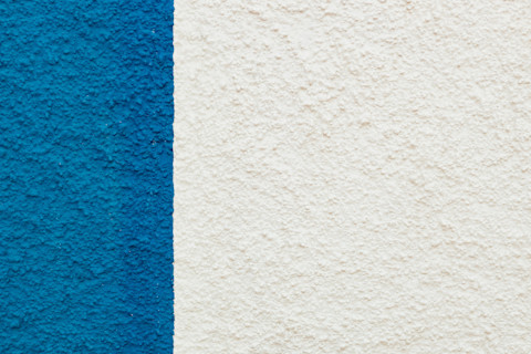 Full-frame shot of a stucco surface, mostly white with one bold blue rectangular section on the left.