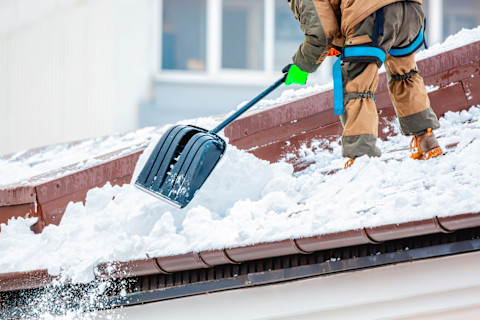 This image shows a tradesperson removing snow from a roof with a shovel.