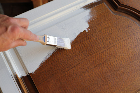 Closeup of a brown wooden kitchen cabinet being painted white.
