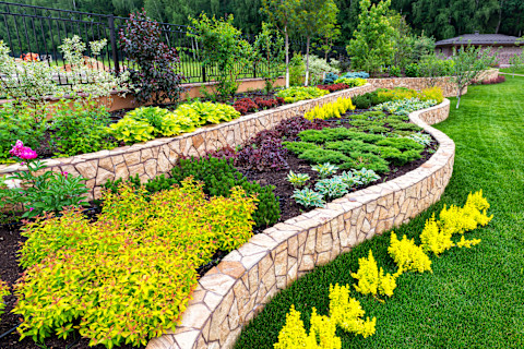 A beautiful border in a yard with flowers and plants in it on a grass field.