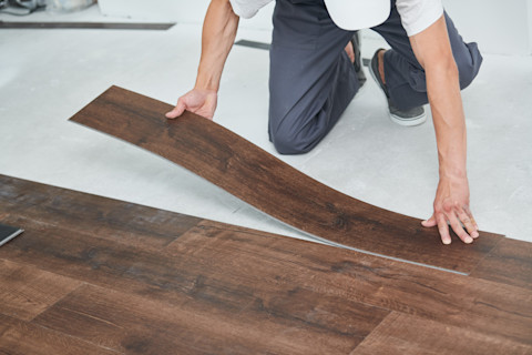 This image shows a flooring fitter installing vinyl flooring that has a hardwood appearance.