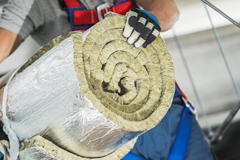 This image shows a construction worker wearing safety gloves carrying a roll of insulation material.