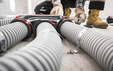 Closeup of a HRV distributor, focus on three hoses. A worker's feet are visible in the back.