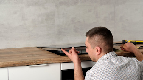 An electrician installs a black induction stove in a wooden countertop.