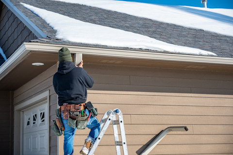 Worker installing white rain gutter along house roof edge