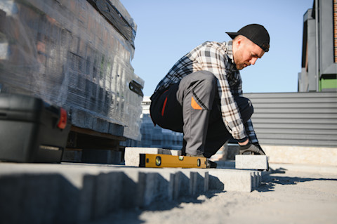 A landscaping worker lays paving stones outdoors. The stones are aligned by hand.