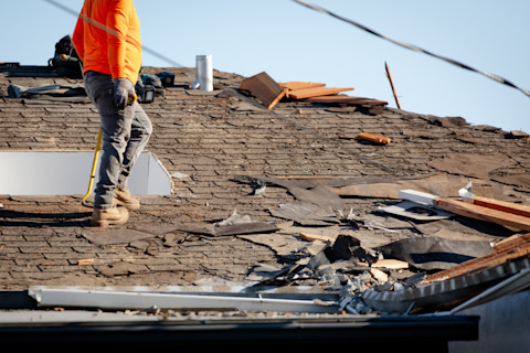 A roof repair pro stands on a roof where a large section has been visibly damaged. Different repair materials are spread out across the roof.