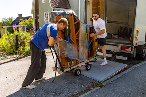 Two professional movers use a moving dolly to load a piano onto a moving truck.