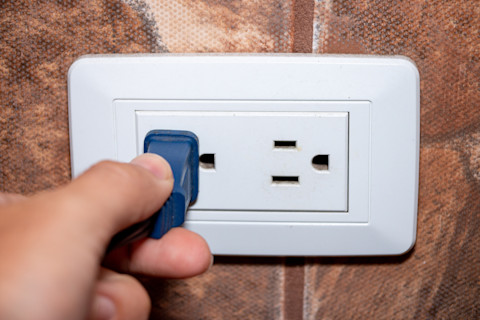 closeup of someone’s hand plugging a Type A plug into an electrical socket.