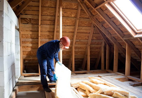 Roof insulation. A worker puts glass wool insulation in the attic.