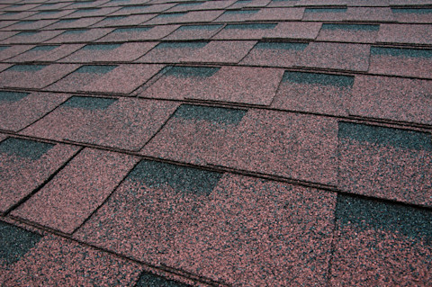 Closeup of a shingled roof. The shingles are mostly brown, though some have a black edge.